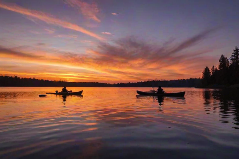 Beautiful sunset over a tranquil lake, with a silhouette of a couple kayaking, the sky ablaze with oranges and purples, creating a romantic and peaceful atmosphere.