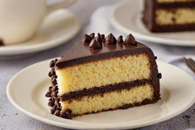 Generate an image of a slice of cake with a light yellow sponge, layered with a creamy filling and speckled with dark chocolate chips. The cake should be presented on a simple plate with a soft background, highlighting its texture and color.