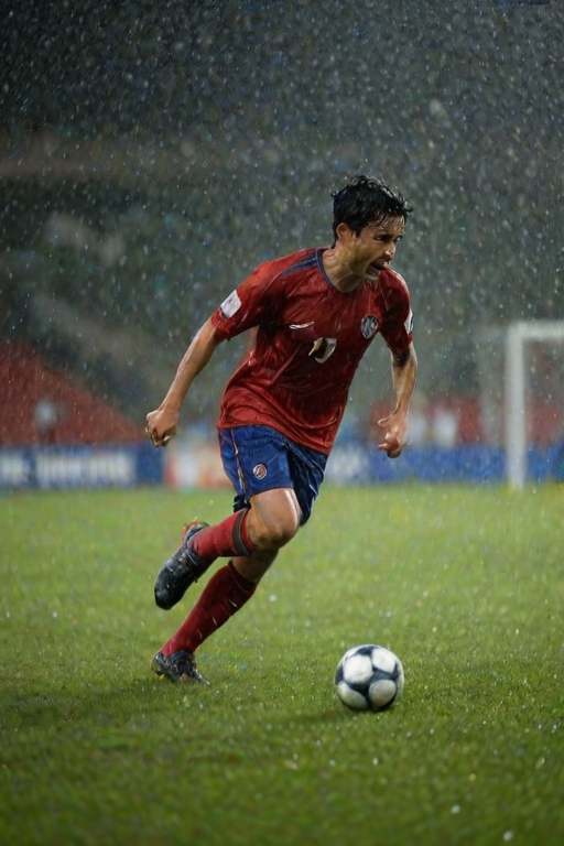 Blurry action shot of a soccer player celebrating a goal on a rain-soaked field, water droplets flying through the air, with distant stadium lights reflecting off the wet grass.