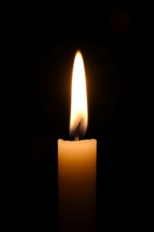 Create an image of a lit candle with a bright, flickering flame against a dark background, using a DSLR camera with a 50mm lens, aperture set to f/1.8 for a shallow depth of field, ISO 100 for minimal noise, and a soft focus effect to enhance the warm glow and surrounding bokeh.