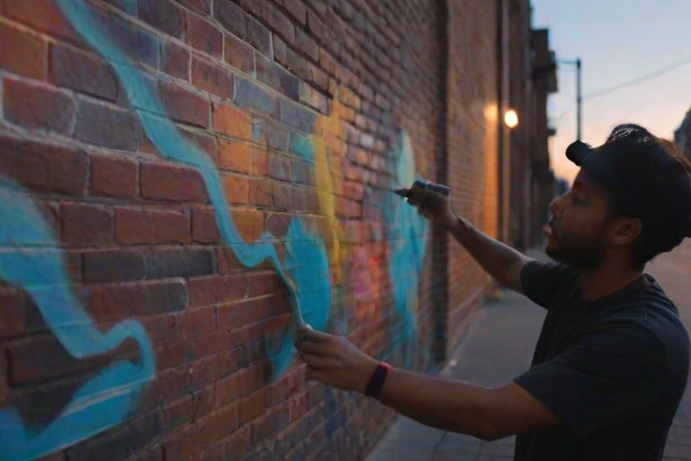 Blurry candid shot of a street artist spray-painting a mural on a brick wall at dusk, vibrant colors blending together, with distant passersby watching and warm light from street lamps casting shadows.