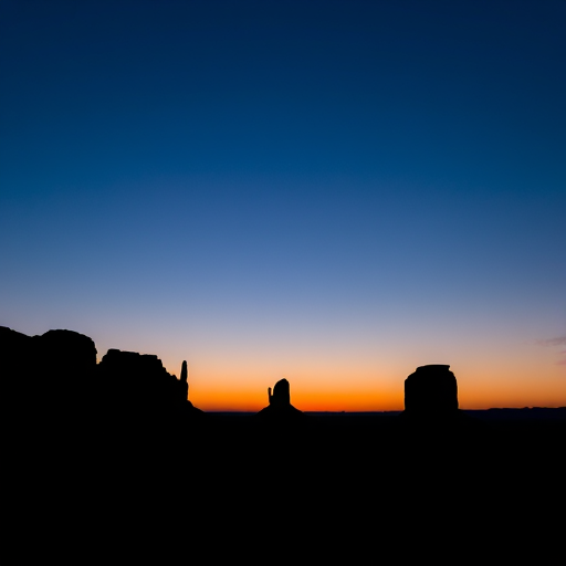 Capture a twilight landscape with silhouetted rock formations against a gradient blue sky, using a DSLR camera with a 24mm lens, aperture f/4, ISO 800, shutter speed 1/30 sec, and a wide angle view for enhanced depth.