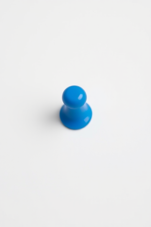 Create a blue map pin with a round black center on a white background, shot with a DSLR camera at f/5.6 aperture, ISO 100, 50mm lens, with a shallow depth of field and natural lighting.