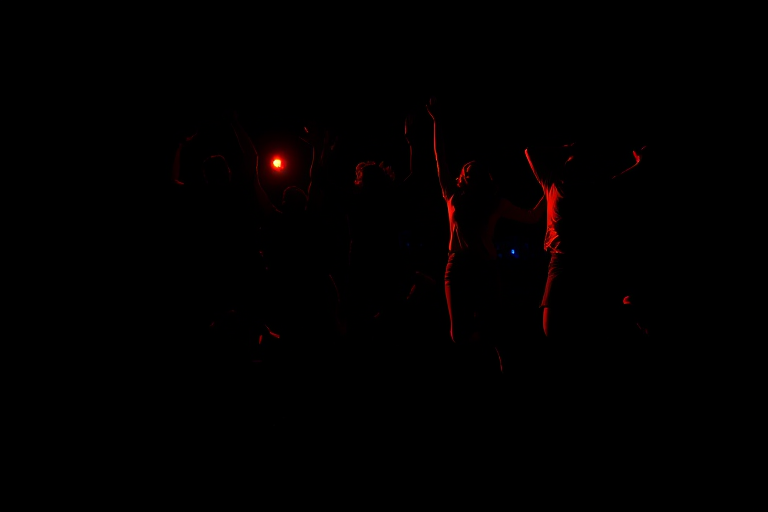 capture a vibrant silhouette of a group of five people jumping joyfully against a black background, using a DSLR camera with a wide-angle lens at f/4, ISO 100, shutter speed 1/250s, in landscape orientation for enhanced quality and depth