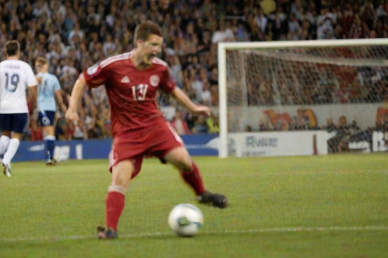 Blurry action shot of a soccer player kicking a ball towards the goal, soft focus on the cheering crowd in the background, with a feeling of excitement and anticipation in the air.