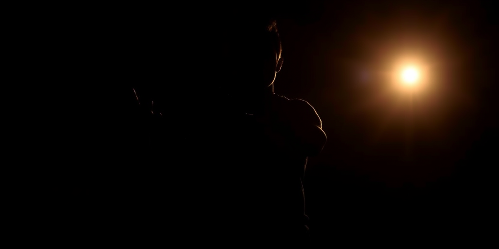 Generate a high-resolution image of a dark silhouette of a person standing with an outstretched hand, captured using a DSLR camera at f/2.8, ISO 100, shutter speed 1/200s, with a shallow depth of field and a backlit setting for dramatic lighting.