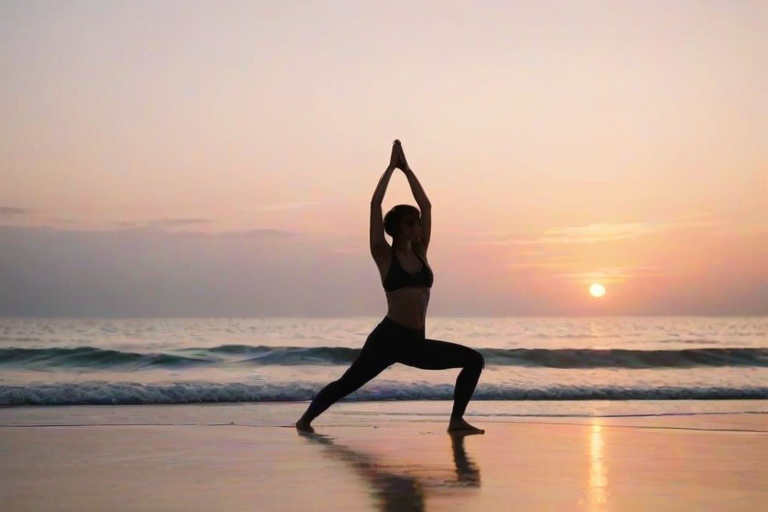 Soft-focus image of a woman practicing yoga on a sandy beach at sunrise, her silhouette framed against the soft pastel colors of the sky, gentle waves lapping at the shore.