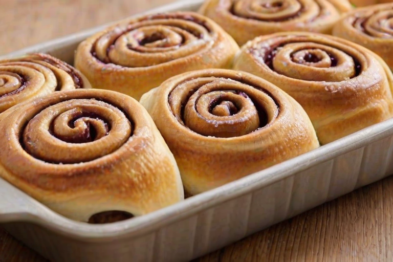 Create an image of freshly baked cinnamon rolls with a rich berry filling. The rolls should be golden brown with a soft, fluffy texture, and dusted lightly with powdered sugar. They should be arranged in a baking tray lined with parchment paper, showcasing their swirled design and inviting appearance. The background should be softly blurred to keep the focus on the delicious rolls.