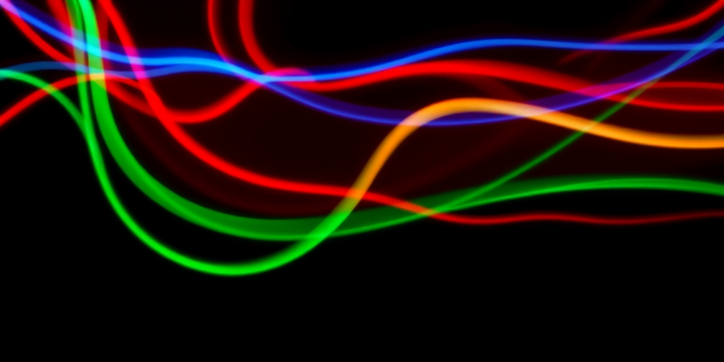 create a vibrant abstract light trails image with smooth flowing lines in red, blue, green, and yellow on a black background, using a DSLR camera with a 50mm lens at f/1.8, shutter speed 1/60s, ISO 100, shot from a low angle and in long exposure style to capture motion and enhance luminosity