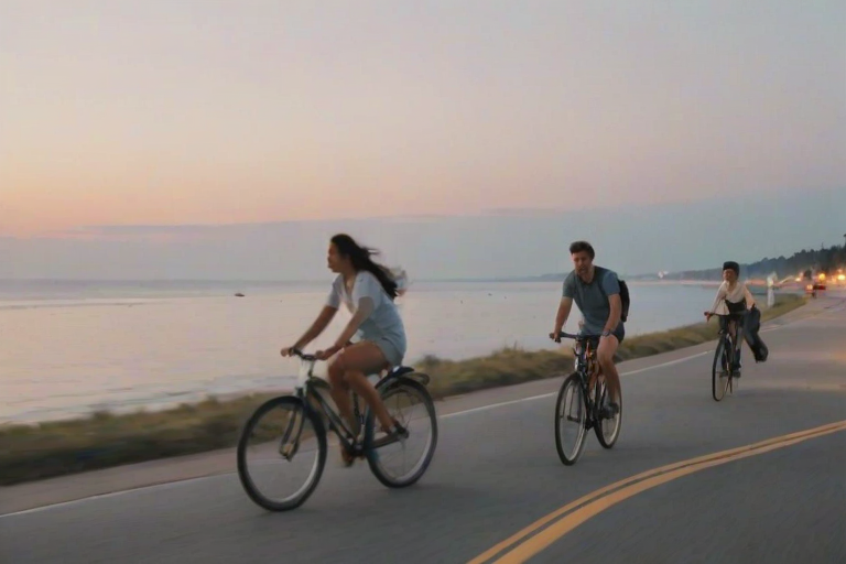 Blurry, candid shot of friends riding bicycles through a coastal town at twilight, soft pastel colors in the sky, distant ocean waves crashing, and the sound of laughter and ringing bells.