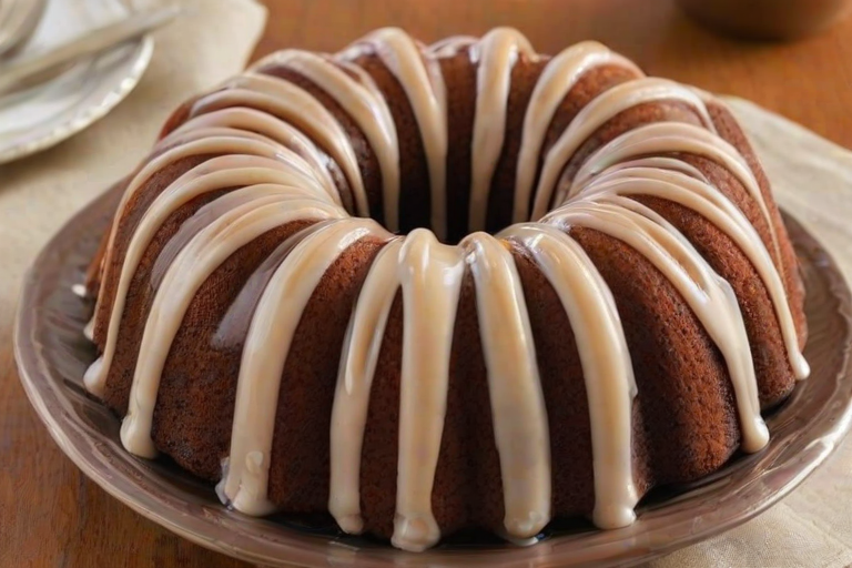 Create an image of a round bundt cake with a smooth, glossy glaze drizzled over the top. The cake should have a light brown color with a white icing that creates a decorative pattern running down the sides. The background should be simple and neutral to highlight the cake.