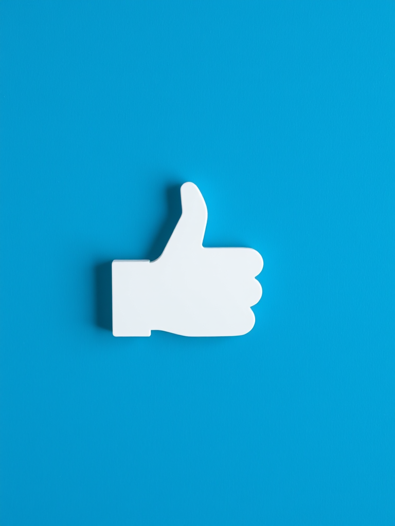 Regenerate an image of a thumbs-up icon on a textured blue background with high resolution, using a Canon EOS R5 with a 50mm f/1.2 lens, aperture f/5.6, ISO 100, 1/125s exposure, top-down view, and soft light.