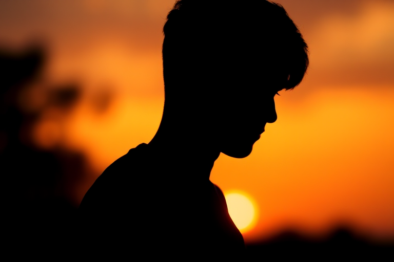 Create a high-resolution silhouette of a figure against a sunset backdrop with soft bokeh; shot with a DSLR camera, 50mm lens, f/1.8 aperture, ISO 100, and a shutter speed of 1/200s in portrait orientation.