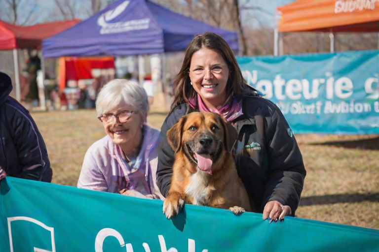 Heartwarming pet adoption event, featuring volunteers with dogs of various breeds, families interacting with the animals, and colorful banners promoting the cause, creating a heartwarming atmosphere.