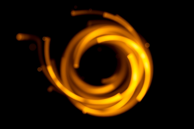 Generate a high-quality image of a glowing golden swirl on a black background using a DSLR camera with a 50mm lens, f/1.8 aperture, ISO 100, 1/200s shutter speed, taken from a close-up view with a soft focus style.