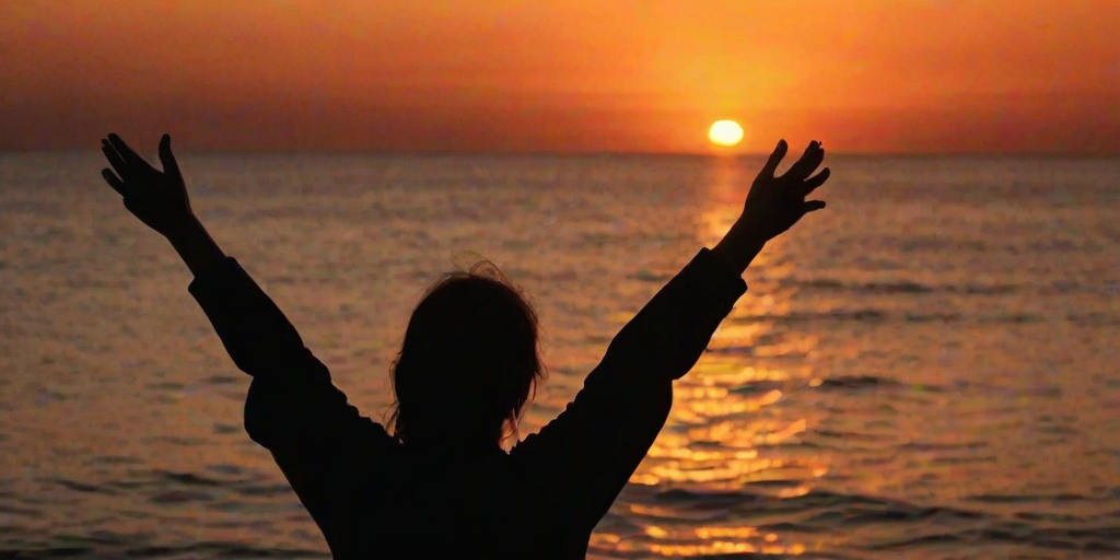 silhouette of a person with outstretched arms against a vibrant orange sunset over the ocean