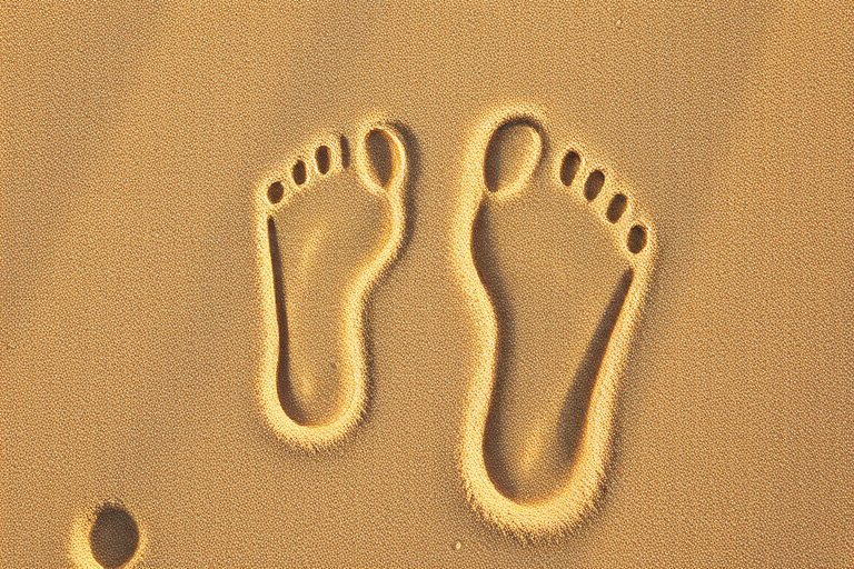 Generate a high-resolution image of two human footprints over a textured sand background, using a DSLR camera with a 50mm lens, aperture set to f/2.8 for shallow depth of field, ISO 100 for clarity, and a slight overhead angle for emphasis on the footprints.