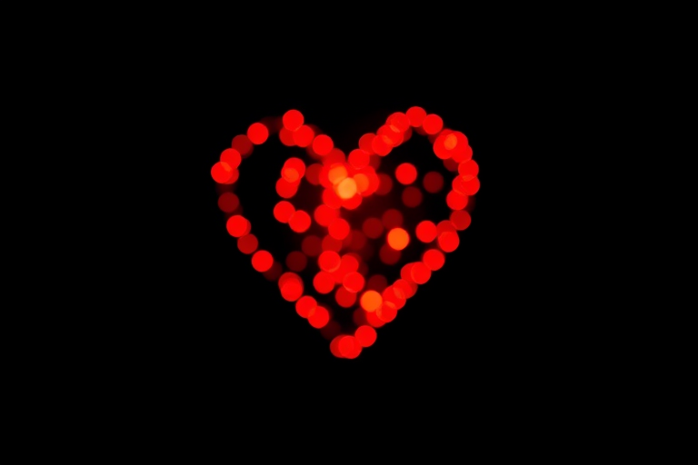 Create a vibrant image of a heart-shaped design made with sparkling red lights on a black background, using a DSLR camera, 50mm lens at f/1.8 aperture, ISO 100, and a shutter speed of 1/60s, with a shallow depth of field to enhance the bokeh effect.