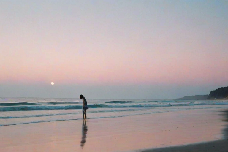 Soft-focus image of a quiet beach at twilight, with gentle waves lapping at the shore, soft pastel colors in the sky, and a single silhouette walking along the water’s edge.