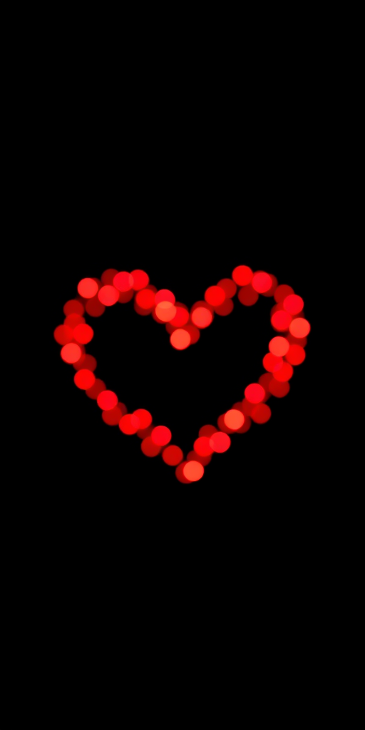 Create a vibrant image of a heart-shaped design made with sparkling red lights on a black background, using a DSLR camera, 50mm lens at f/1.8 aperture, ISO 100, and a shutter speed of 1/60s, with a shallow depth of field to enhance the bokeh effect.