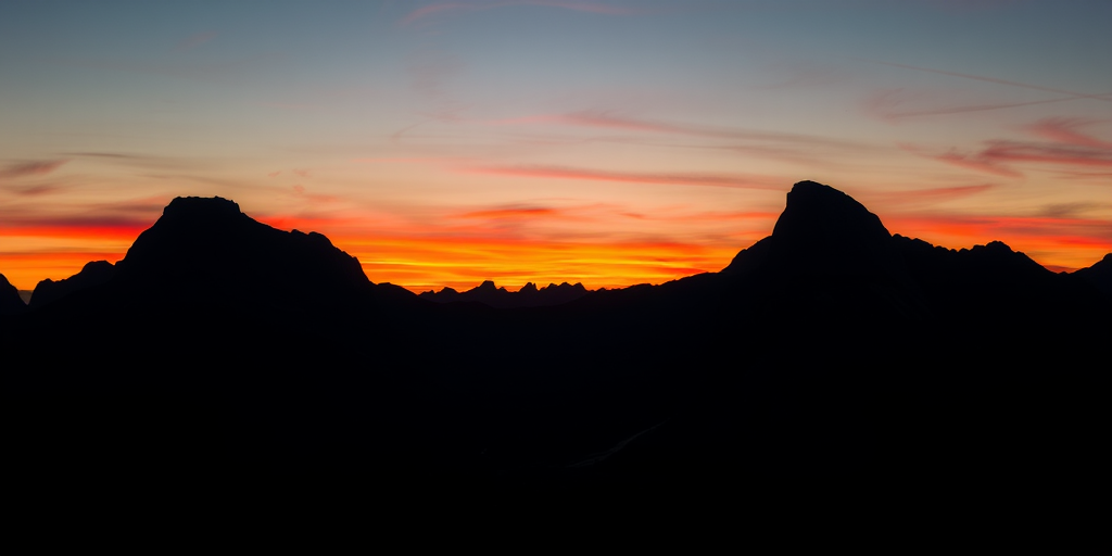Create a high-contrast silhouette of a majestic mountain landscape during sunset, capturing rich colors in the sky, with a camera type of DSLR, lens focal length of 35mm, aperture set to f/8, shutter speed at 1/250s, and ISO 100, viewed from a wide-angle perspective.