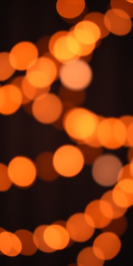 Create a high-resolution image of a bokeh background with soft, glowing orange and white lights against a dark backdrop, using a DSLR camera with a 50mm lens at f/1.8, ISO 100, and a shutter speed of 1/50s, captured in portrait mode for a smooth depth of field and vibrant colors.