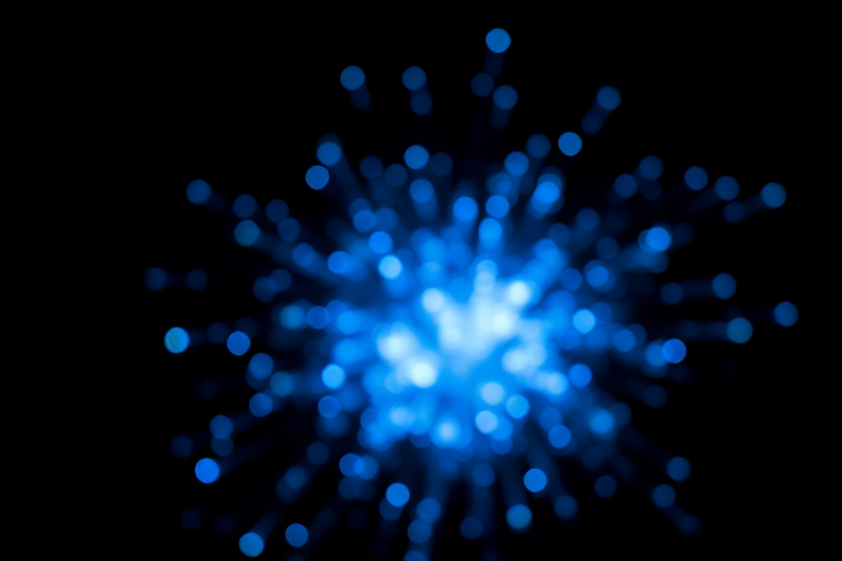 Create an abstract explosion of blue light on a black background, captured with a DSLR camera at f/1.8, ISO 200, shutter speed 1/60s, using a macro lens for sharp detail and a soft bokeh effect.
