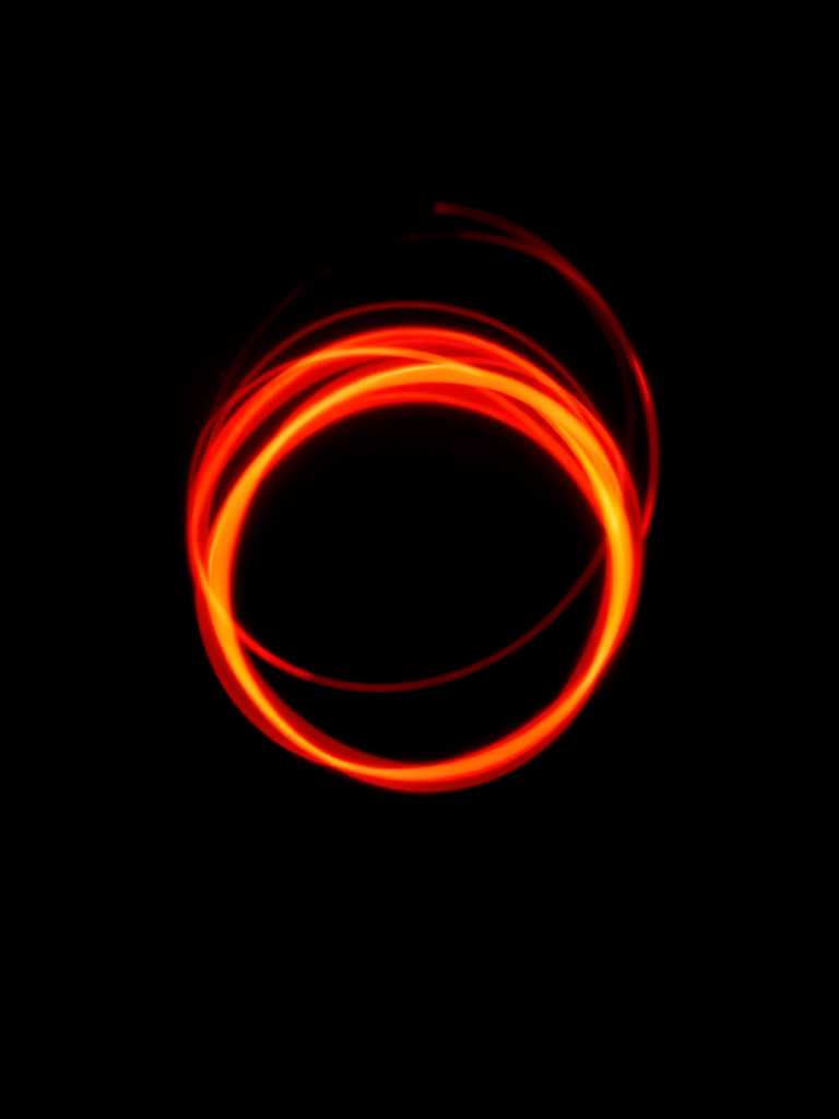 Create a radiant orb with swirling red and orange light spirals on a black background, using a Canon EOS R camera with a 50mm lens, aperture f/1.8, ISO 100, shutter speed 1/60 sec, shot from a close-up perspective with a high-contrast setting.