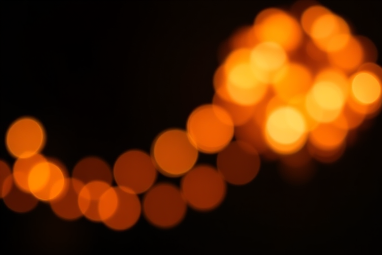 Create a high-resolution image of a bokeh background with soft, glowing orange and white lights against a dark backdrop, using a DSLR camera with a 50mm lens at f/1.8, ISO 100, and a shutter speed of 1/50s, captured in portrait mode for a smooth depth of field and vibrant colors.