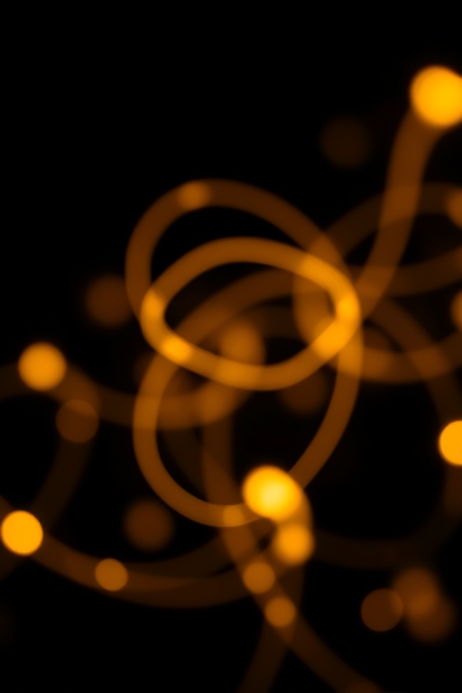 Create a high-resolution abstract artwork of soft golden light swirls on a black background, captured with a Canon EOS 5D Mark IV, 50mm lens, aperture f/1.8, ISO 100, and a shutter speed of 1/125s, using a shallow depth of field to emphasize the luminous trails.