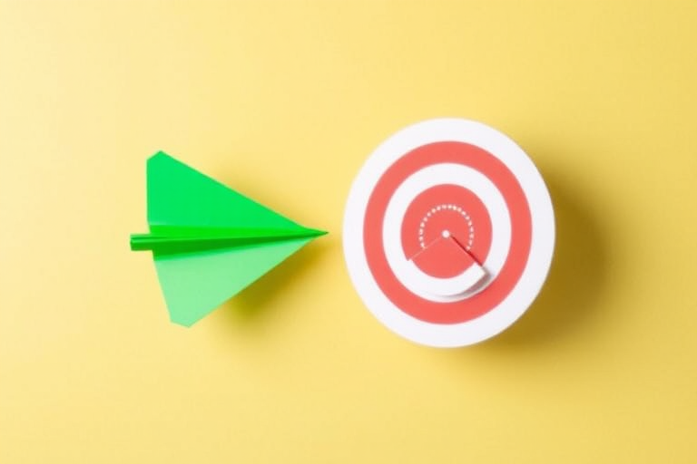 create a minimalist design of a green paper airplane flying towards a red and white target on a light yellow background, focus on vibrant colors and sharp contrasts, use a DSLR camera with f/4 aperture, ISO 100, 50mm lens, and a top-down view to enhance image quality