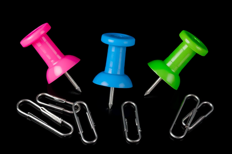 Create a vibrant illustration of three colored thumbtacks (pink, blue, green) surrounded by silver paperclips on a black background, using a digital art style with high contrast, 4K resolution, and a lightbox effect for added depth, simulating a Canon EOS 5D Mark IV with a 50mm f/1.8 lens at f/8, ISO 100, and 1/250 sec shutter speed.
