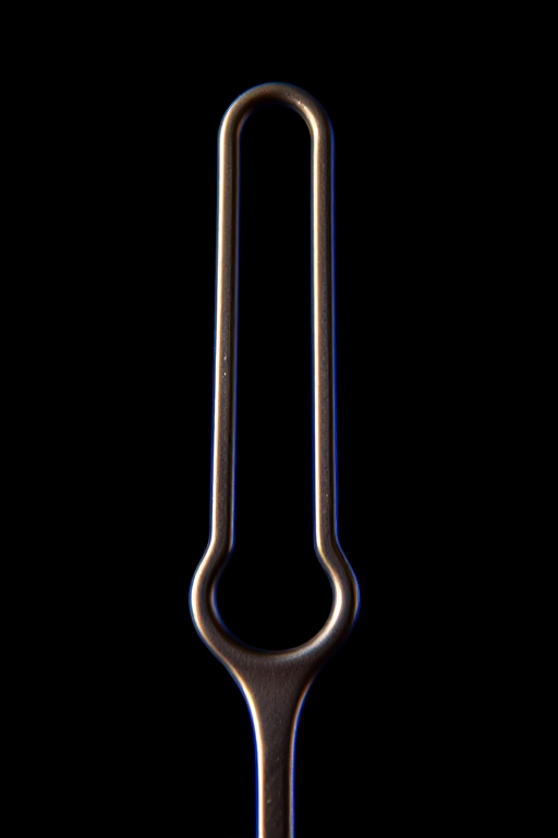 Create a close-up image of a metallic tuning fork against a black background with dramatic blue lighting, using a DSLR camera at f/4 aperture, 1/200 sec shutter speed, ISO 100, and a 50mm lens to capture fine details.