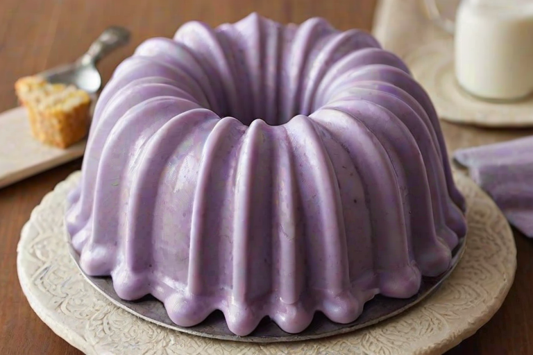 Create an image of a cake in a bundt pan, featuring a mix of light purple and white layers. The cake should be resting on a neutral-colored cloth, with an ice cream scoop placed beside it. The background should have a simple, textured surface to enhance the focus on the cake.