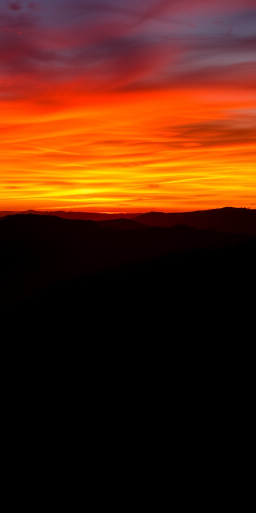 Create a vibrant sunset landscape with a silhouette of mountains in the foreground, captured with a Canon EOS R5, 24mm focal length, f/8 aperture, ISO 100, HDR settings for dynamic range, wide-angle view, and enhanced color saturation.