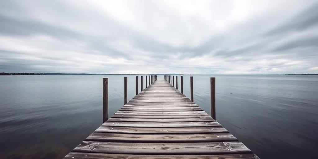 A serene view of a wooden pier extending into calm water, under a moody overcast sky, captured with a DSLR camera, 35mm lens, f/8 aperture, ISO 200, shot from a low angle to emphasize depth and perspective.