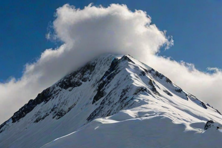 mountain peak covered in snow with clouds surrounding the summit under a bright blue sky