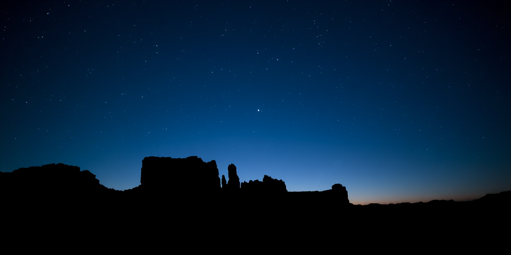 Capture a serene twilight landscape silhouette with rocky formations against a deep blue sky filled with stars, using a DSLR camera at ISO 800, f/4.0 aperture, 15-second exposure, and a wide-angle lens at 18mm for enhanced clarity and depth.