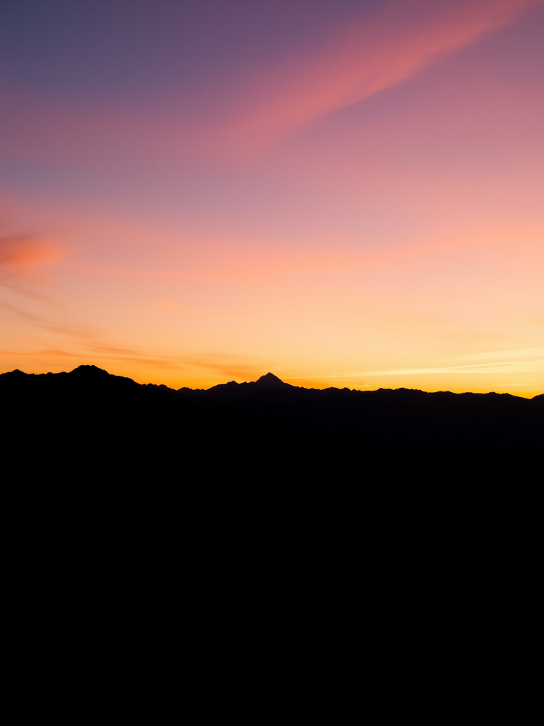 Generate an image of a minimalist landscape featuring a silhouette of mountains at sunset, using a Canon EOS R5 with a 50mm lens, aperture set to f/8, ISO 100, with a panoramic view and soft lighting to enhance the colors in the sky.