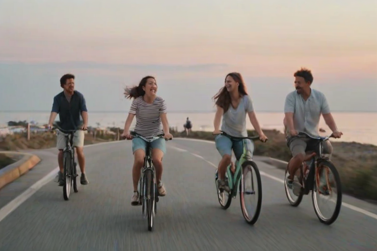 Blurry, candid shot of friends riding bicycles through a coastal town at twilight, soft pastel colors in the sky, distant ocean waves crashing, and the sound of laughter and ringing bells.