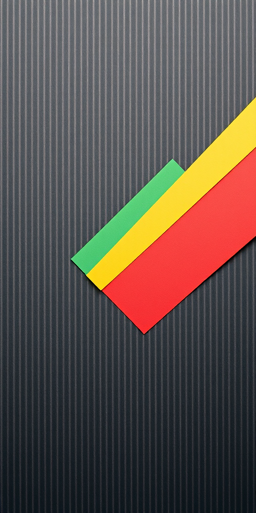 Create an abstract design featuring a diagonal strip of colored paper (green, yellow, red, and white) on a textured dark gray striped background, captured with a Canon EOS R5, 50mm lens, f/1.8, ISO 100, with a shallow depth of field and soft lighting for enhanced contrast and clarity.