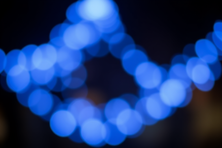 Create an image of bokeh lights in various shades of blue on a dark background, using a 50mm lens at f/1.8, ISO 200, shutter speed 1/60s, shot from a shallow depth of field perspective, in high-resolution digital format.